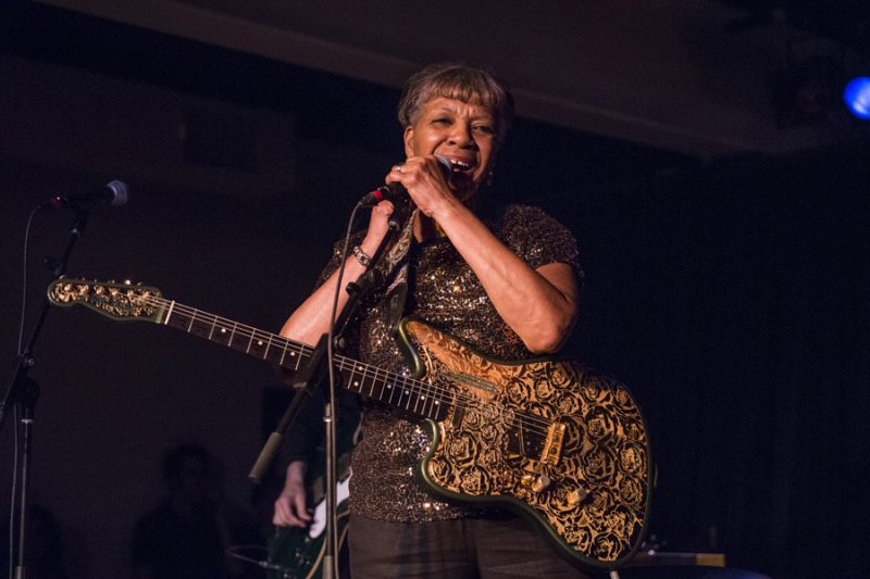 A woman holding a microphone and guitar in front of a crowd.